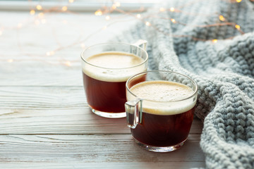 Two cups of coffee, warm knitted sweater on wooden background. Warm lights. Cozy winter morning. Lifestyle concept. Selective focus.