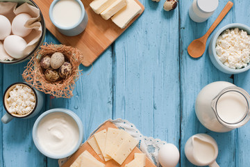 Different types of dairy products on blue wooden background: milk, sour cream, cottage cheese, cheese, cream, yougurt, butter and eggs. Top view with copy space
