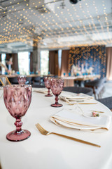 Wedding Banquet or gala dinner. The chairs and table for guests, served with cutlery and crockery. Covered with a pastel pink tablecloth runner. party lighted with garlands
