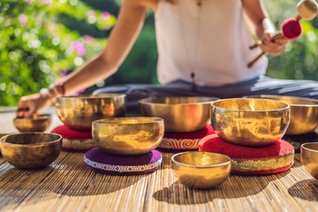 Woman playing on Tibetan singing bowl while sitting on yoga mat against a waterfall. Vintage...