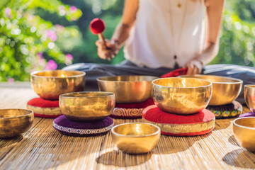 Woman playing on Tibetan singing bowl while sitting on yoga mat against a waterfall. Vintage tonned. Beautiful girl with mala beads meditating