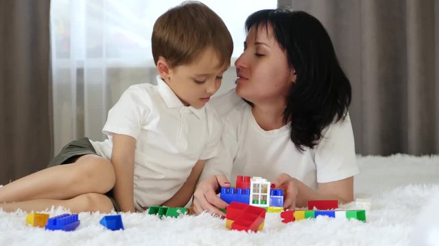 The concept of mother-child relationship. Happy baby and mom are playing meccano while lying on the couch. A mother kisses her son.