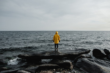 man in a yellow rain coat stands on the shore of the blue sea