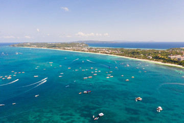 Many tourist boats near the island of Boracay. Seascape in the Philippines in sunny weather, view from above. A large densely populated island with hotels and a white beach.