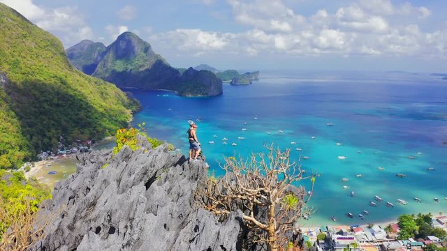 Hikers couple standing on top of a mountain and enjoying blue lagoon bay view in El Nido, Palawan, Philippines. Aerial view 4K