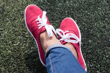 young woman's feet in red sport shoes on grass field