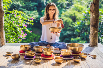 Woman playing on Tibetan singing bowl while sitting on yoga mat against a waterfall. Vintage...