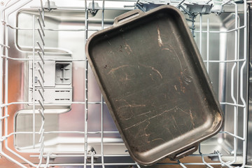 Black baking sheet lies in the lower compartment of the dishwasher