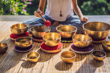 Woman playing on Tibetan singing bowl while sitting on yoga mat against a waterfall. Vintage...