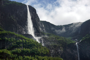 Travel to Norway, a waterfall flows from the top of a high mountain against a cloudy sky