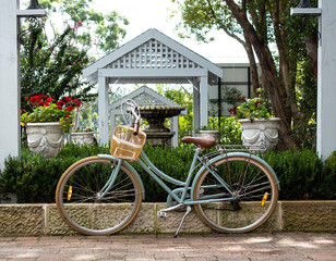 Retro ladies bicycle with basket standing against garden retaining brick wall with lush green shrubs in background