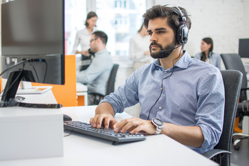 Young handsome male customer support phone operator with headset working in call center.