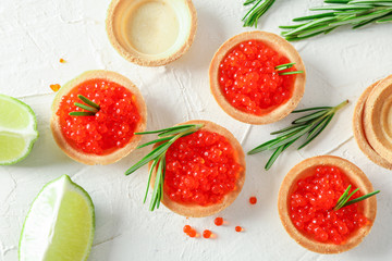 Tartlets with caviar, rosemary and limes on white background, top view
