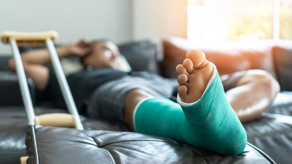 Bone fracture foot and leg on male patient with splint cast and crutches during surgery rehabilitation and orthopaedic recovery staying at home - obrazy, fototapety, plakaty