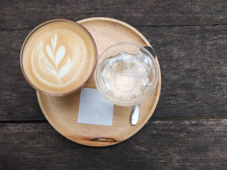 Cup of coffee with heart latte art close-up, spoon and glass of water on light wooden plate