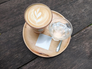 Cup of coffee with heart latte art close-up, spoon and glass of water on light wooden plate