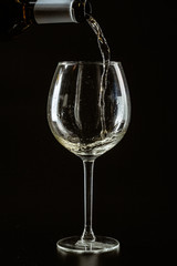 White wine being poured in a wine glass on a dark background