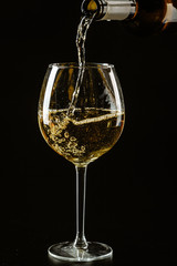 White wine being poured in a wine glass on a dark background