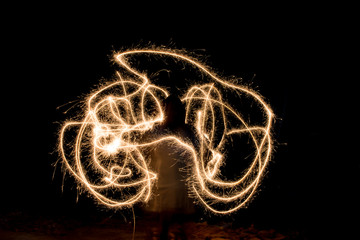 Unknown young girl playing with sparklers - shot with slow shutterspeed revealing abstract light trails over black background.