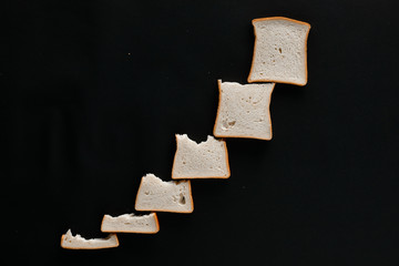 A line of slices of bread which are getting bigger and bigger, on a black background, shot from...