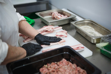 The process of preparing meat products. Gloved hands are molded from ground beef and bacon patties