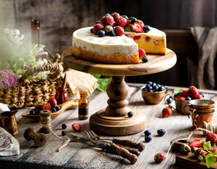 Homemade raspberry sliced biscuit cake with white cream and berries on top on wooden cake stand