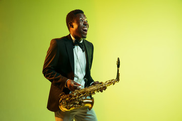 Young african-american jazz musician playing the saxophone on gradient yellow-green studio...