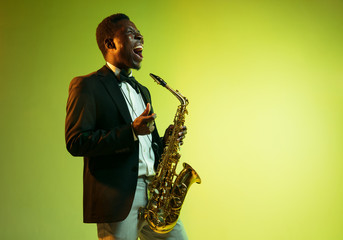 Young african-american jazz musician playing the saxophone on gradient yellow-green studio...