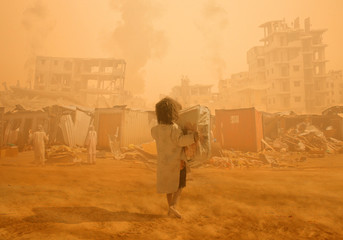 Homeless little girl walking in destroyed city that was bombed by the enemy and she's looking for shelter. - obrazy, fototapety, plakaty