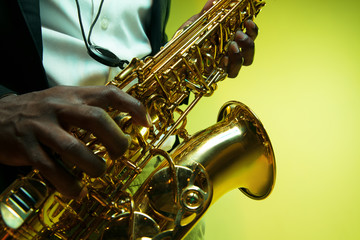 Young african-american jazz musician playing the saxophone on gradient yellow-green studio...