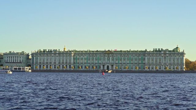 A boat floating left to right on Neva river on background of Winter Palace in Saint Petersburg in spring. Calm weather and clear blue sky with no clouds