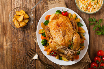 Roast chicken whole. Served on a plate with vegetables and baked potatoes.