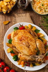 Roast chicken whole. Served on a plate with vegetables and baked potatoes.