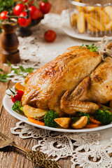 Roast chicken whole. Served on a plate with vegetables and baked potatoes.