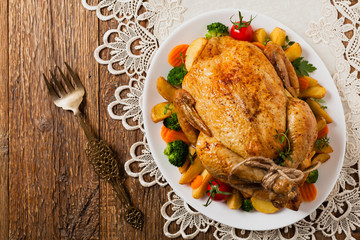 Roast chicken whole. Served on a plate with vegetables and baked potatoes.