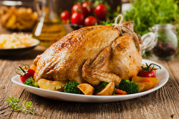 Roast chicken whole. Served on a plate with vegetables and baked potatoes.