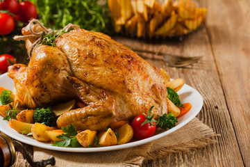 Roast chicken whole. Served on a plate with vegetables and baked potatoes.
