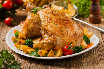 Roast chicken whole. Served on a plate with vegetables and baked potatoes.