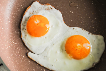 Fried eggs in a pan and raw eggs are on the table
