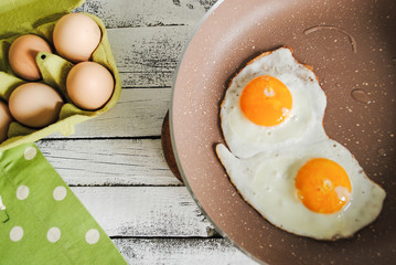 Fried eggs in a pan and raw eggs are on the table