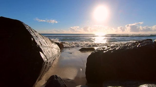 Shimmering golden sunset, waves lapping on sand, wide veiw between Black rocks