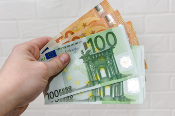 Hand with euro banknotes upon white brick wall close up