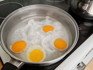 Poaching fresh eggs in a pan of water in an authentic kitchen environment. Four eggs part way...