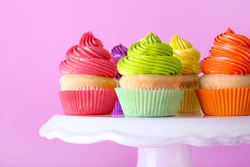 Stand with sweet tasty cupcakes on color background