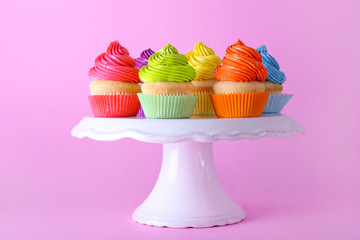 Stand with sweet tasty cupcakes on color background