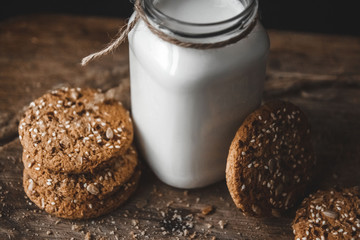 Cereal cookies with a jug of milk on a wooden background.