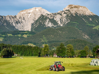 Traktor düngt ein Feld in den Alpen