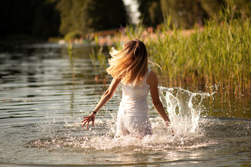 slender girl with blond hair dancing in the water at sunset and splashing water. The concept of freedom, happiness, love