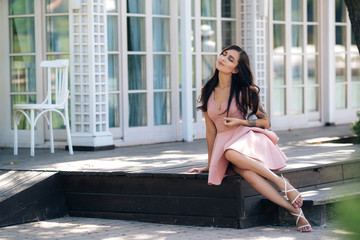 Obraz na płótnie Canvas Beautiful sexy girl in pink dress posing on wooden steps of street cafe