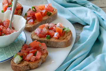 Top view of woman hands preparing tasty tomato Italian appetizers -  bruschetta, on slices of toasted baguette, close up view